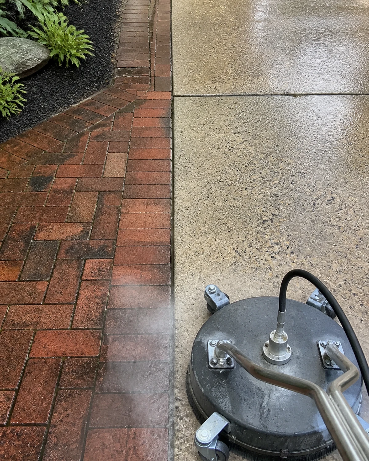 Concrete driveway edge being cleaned beside a brick walkway